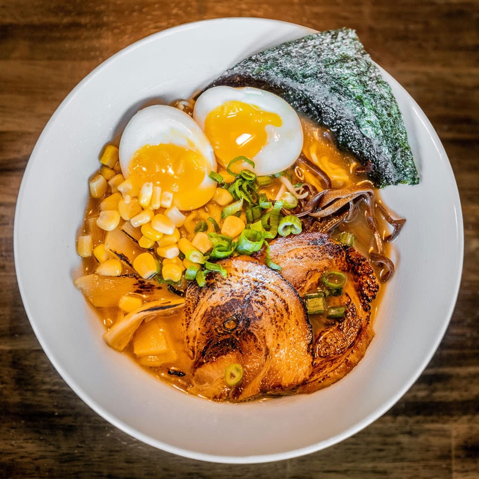 Miso ramen bowl with pork belly, soft-boiled eggs, corn, green onions, and nori.