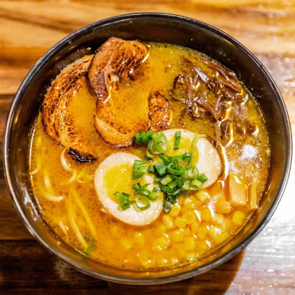 A bowl of Miso ramen with pork, corn, green onions, and a soft-boiled egg.