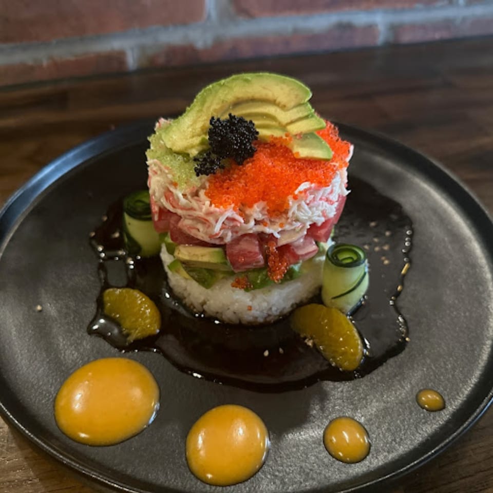 A vibrant Miso sushi tower with avocado, caviar, crab, tuna, and rice, garnished with sauce.