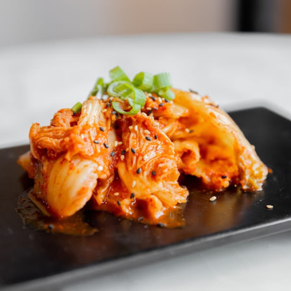 Spicy kimchi, garnished with green onions and sesame seeds, on a black rectangular plate.