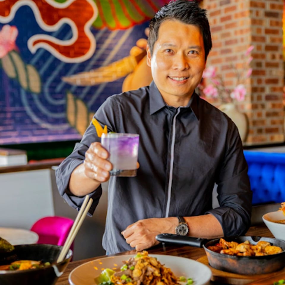 A man in a black shirt holding a purple cocktail, surrounded by Japanese dishes at Miso.